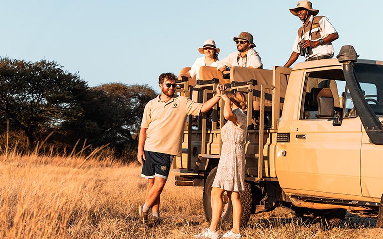 Guests standing in the savannah next to a car on a safari game drive in the morning at